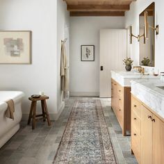 a long hallway with wood ceilinging and white walls, leading to a large bathroom