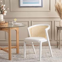 a white chair sitting next to a table with a vase on it and flowers in the corner