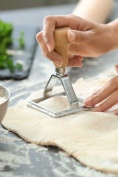 two hands are rolling dough on a table