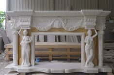 a white marble fireplace surround with statues on the mantle and around it is being worked on