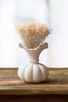 a white vase filled with dried flowers on top of a wooden table