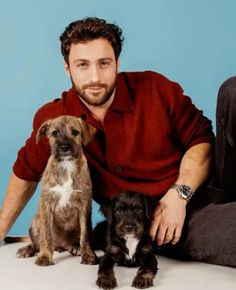 a man sitting on the floor with three dogs in front of him and smiling at the camera