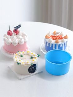 three cakes sitting on top of a white table next to each other and one is blue