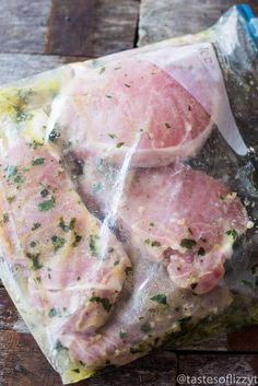 raw meat wrapped in plastic sitting on top of a wooden table next to a knife