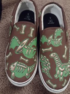 a pair of brown and green shoes with skeleton drawings on the side, sitting on carpet