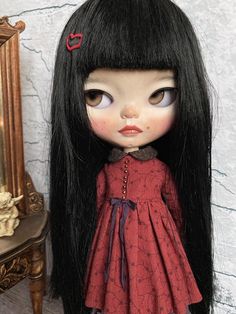 a doll with long black hair wearing a red dress next to a table and mirror