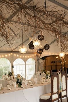 a dining room with tables and chairs covered in white tablecloths, lights and branches