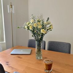 a wooden table topped with a laptop computer next to a vase filled with yellow flowers