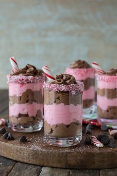 three glasses filled with desserts on top of a wooden board next to candy canes