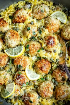 a skillet filled with pasta, meatballs and lemon wedges on the side