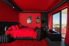 a bedroom with red walls, black furniture and a large window that looks out onto the city