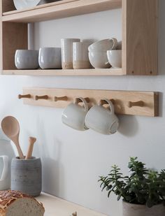 a wooden shelf with cups and spoons on it next to a loaf of bread