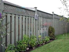 a fence that has some plants growing on it and flowers in the grass behind it