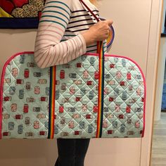 a woman holding a quilted purse in front of a wall with pictures on it