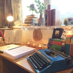 an old typewriter sitting on top of a wooden desk next to books and candles