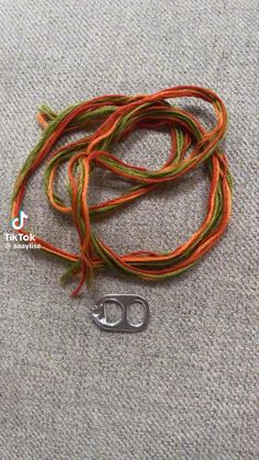 an orange and green cord with a metal hook on the end is laying on a gray surface