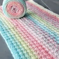 a ball of yarn sitting on top of a multicolored crocheted blanket