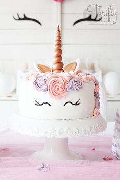 a white cake with pink flowers and a unicorn's horn on top, sitting on a table