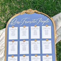 a blue and gold wedding seating chart on the grass with white fabric draped around it