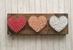 three heart shaped string art pieces on a wooden board