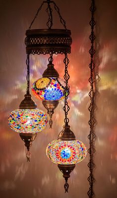 three colorful lights hanging from chains in a room with light shining on the wall behind them