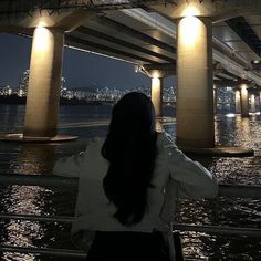 a woman standing on the side of a river under a bridge with lights at night