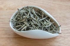 a white spoon filled with green tea on top of a wooden table