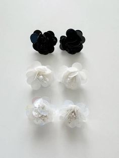 four pieces of black and white flower hair clips on a white surface with one piece being held in the other