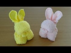 two small stuffed animals sitting next to each other on a wooden table, one is yellow and the other is pink