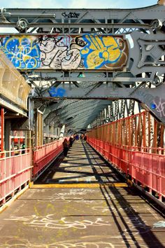 the walkway is covered in graffiti and has red railings on both sides that lead to an overpass