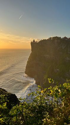 the sun is setting over an ocean cliff