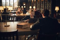 people sitting at tables in a library with laptops and books on the table,