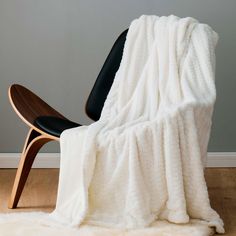 a white blanket sitting on top of a wooden chair next to a black leather chair