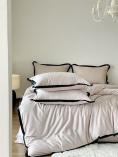 a bed with white sheets and black trim on it in a bedroom next to a chandelier