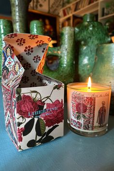 two candles sitting on top of a table next to some vases and boxes with flowers