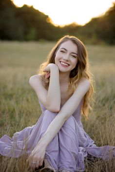 a woman sitting in the middle of a field with her hands on her head and smiling