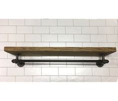 a wooden shelf sitting on top of a white tiled wall next to a black pipe