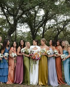 a group of women standing next to each other holding bouquets in front of trees