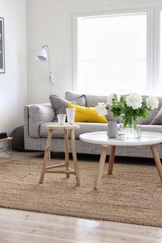 a living room with two tables and a couch in front of a window, the table has flowers on it