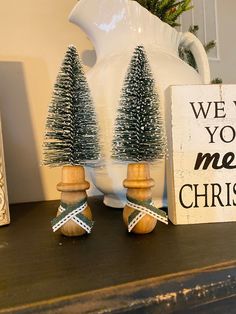 two small christmas trees sitting on top of a wooden table next to a sign that says, we wish you merry christmas