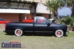 a black pick up truck parked in front of a building with red and white rims