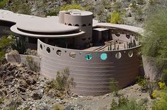 an aerial view of a house in the desert with trees and bushes around it, surrounded by mountains