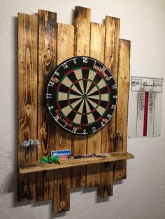 a dart board mounted to the side of a wooden wall next to a shelf with darts on it