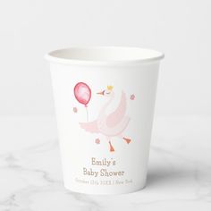 a baby shower cup with a pink swan holding a balloon on it's side