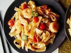 two black plates filled with pasta and vegetables next to utensils on a table