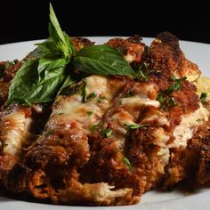 a white plate topped with lasagna covered in sauce and cheese, garnished with green leaves