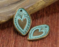 two heart shaped pendants sitting on top of a wooden table next to a piece of wood