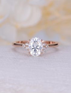 a close up view of a diamond engagement ring on a white surface with flowers in the background