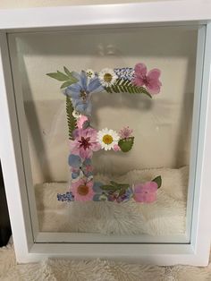 the letter e is made up of flowers and leaves in a shadow box on a white furnishing