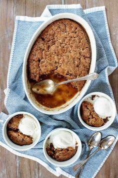 baked dessert in a bowl with ice cream and spoons on a blue towel next to it